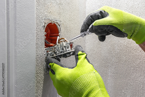 Repairing a damaged light switch, an electrician wearing protective gloves unscrews the switch housing,