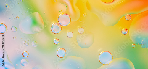 Macro photograph of water droplets against a bright background with smooth transitions of yellow, green, orange, and blue colors. texture is fluid, with bubbles of various sizes, light accents. Banner