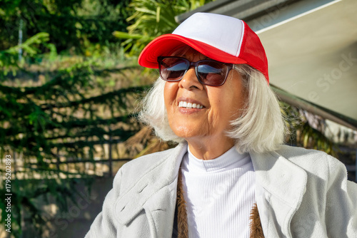 Smiling senior woman wearing sunglasses and red cap outdoors on a sunny day