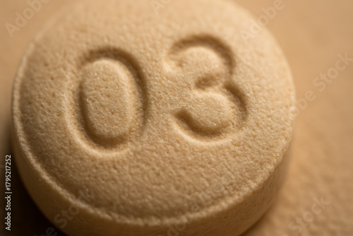 A detailed macro photo of a beige tablet featuring engraved numbers, showcasing the pill’s texture, manufacturing precision, and pharmaceutical identification marks.
