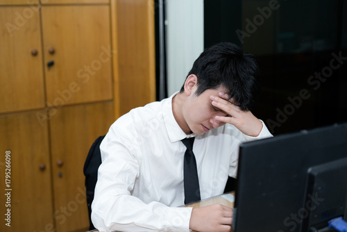 Принти на полотні A stressed Asian office worker or businessman sitting at his desk, burying his f
