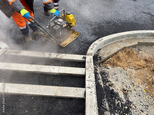 Roadworker compacted hot asphalt with vibratory roller. Laying new asphalt road pavement, road construction workers