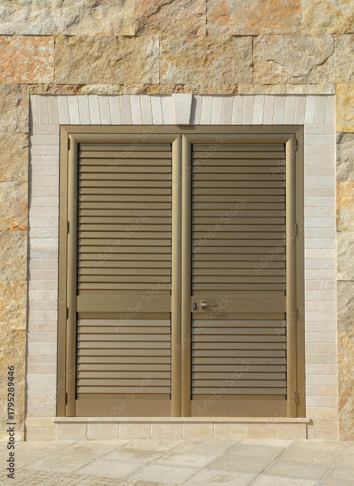 Fototapeta premium Aluminum yellow closed louvered door on sotne wall closeup