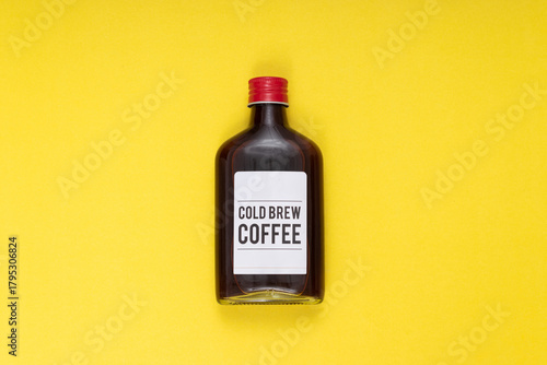 cold brew coffee bottle on yellow background, minimalist composition