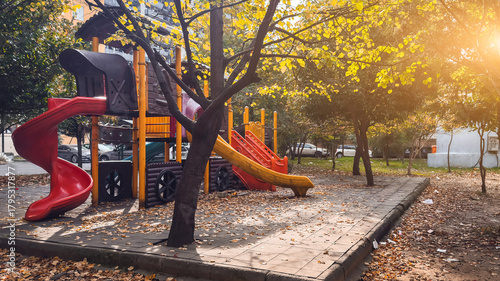 Colorful playground with slides surrounded by autumn trees and warm sunlight creating a peaceful outdoor atmosphere