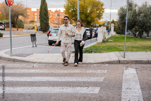 Young visually impaired man crossing street with white cane and assistance