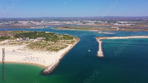 Aerial view drone shot of Tavira Portugal Algarve aerial pier framed view of lagoon and sandy headland with small boat approaching channel leisure boater and shoreline visitors, clear