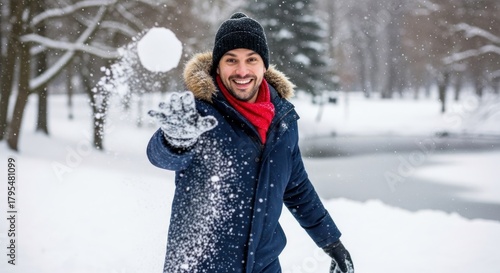 A man in a winter coat throwing a snowball in a snowy park.