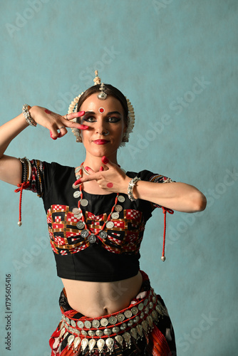 An Indian dancer girl poses in a dance pose in a studio on a blue background