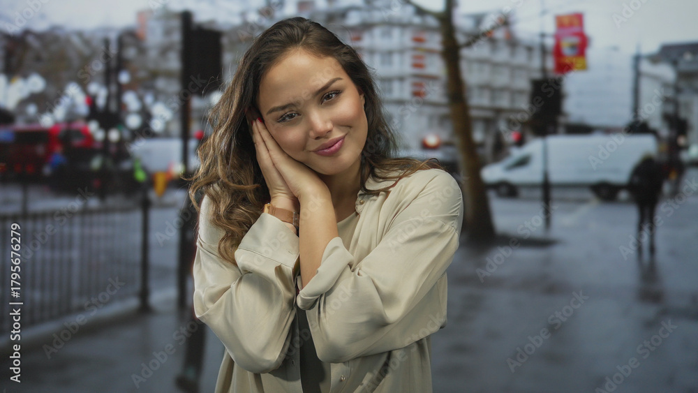 Fototapeta premium Hispanic woman in beige shirt rests head on hands on wet street beneath blurred traffic lights; serenity.