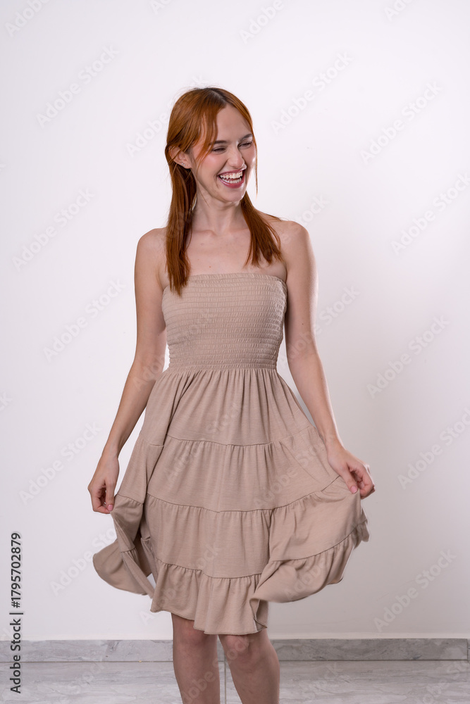 Naklejka premium Red-haired woman posing in beige dress with slight movement, graceful and natural studio portrait.