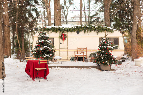 Cozy mobile rv home camping winter. Travel by car. Exterior design travel trailer or recreational vehicle with Christmas decorations, with garden furniture, Xmas tree, chair and table in snow yard. 