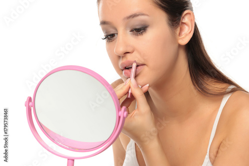 Studio shot of a young woman applying lip liner while looking in a mirror on a white background
