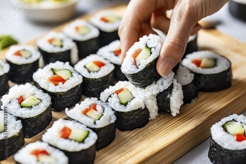 Hand picking fresh sushi rolls with vegetables on bamboo board
