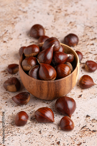 Autumn raw chestnuts in rustic wooden bowl on beige stone kitchen table background, close up
