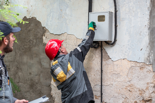 Canvas-taulu Two electricians open the door of a cabinet containing an electric meter to chec
