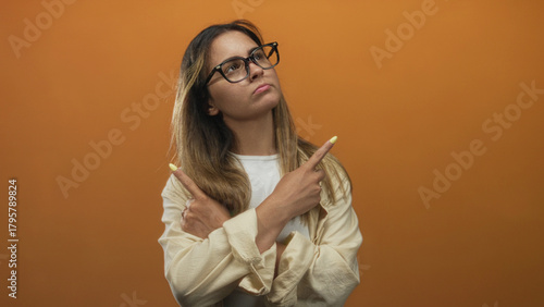 Woman crossing arms and pointing fingers showing yellow nails in studio with orange backdrop; defiance.