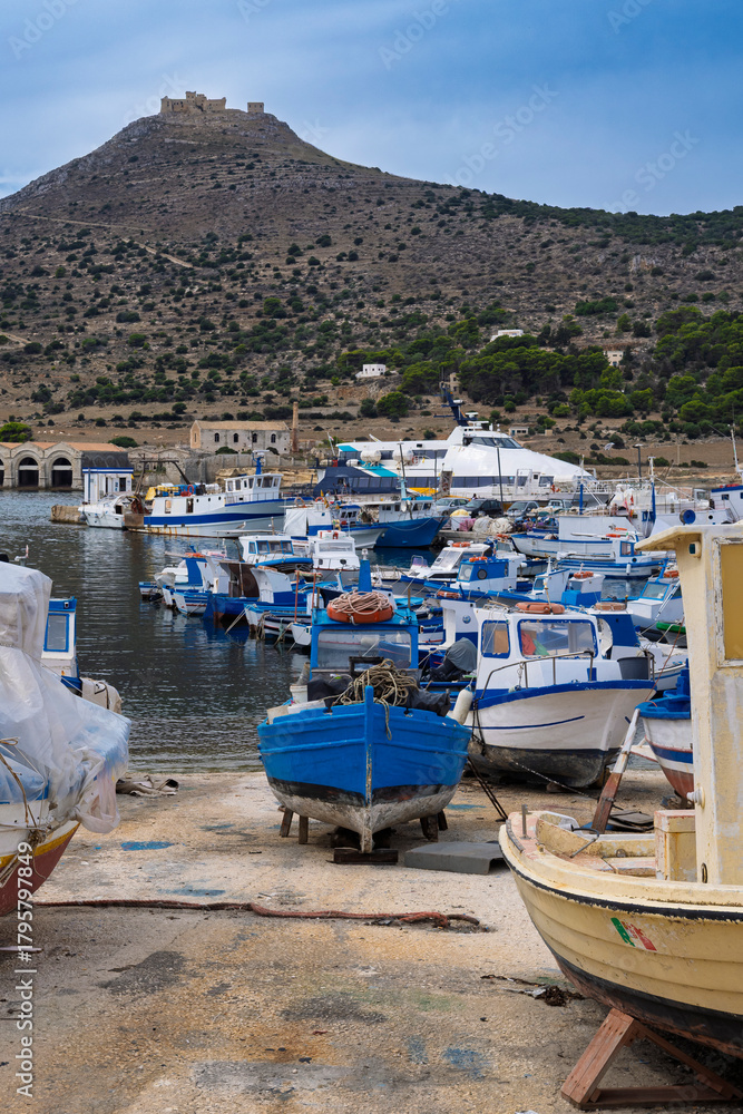 Fototapeta premium The port of the island of Favignana with the traditional wooden fishermen's boats and, in the background, the Castle of Santa Caterina, perched on the top of the hill. Trapani province, Sicily, Italy