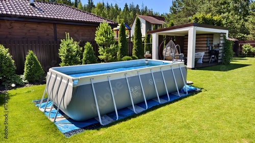 Foto On the mowed lawn stands a gray PVC rectangular frame pool with a coverlet and ladder