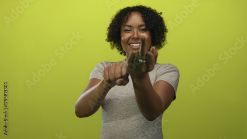 Woman showing middle finger and clenched fist in bright green studio setting; rebellion defiance protest.