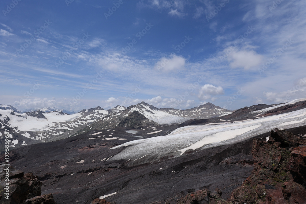 Obraz premium A Majestic View Of A Melting Glacier, Volcanic Slopes, And Snow-Capped Peaks Under A Blue Sky With Clouds.