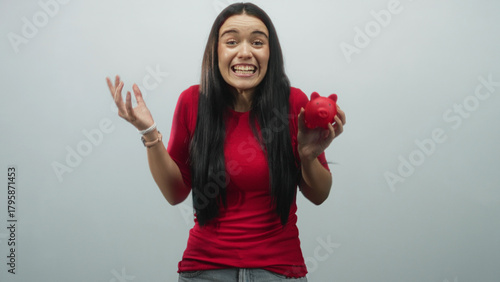 Schilderij op canvas Young woman holding red piggy bank with right hand and pumping left fist, smiling broadly in studio; saving success joy