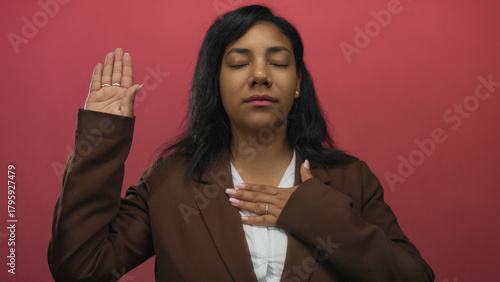 Tableau sur toile African american woman raises hand and touches chest with eyes closed in pink studio; pledge sincerity