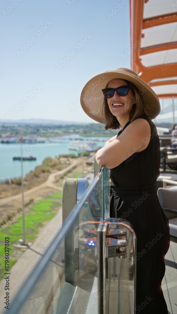 Obraz premium Woman smiling leaning on glass railing on cruise deck overlooking harbor and coastline; serenity vacation.