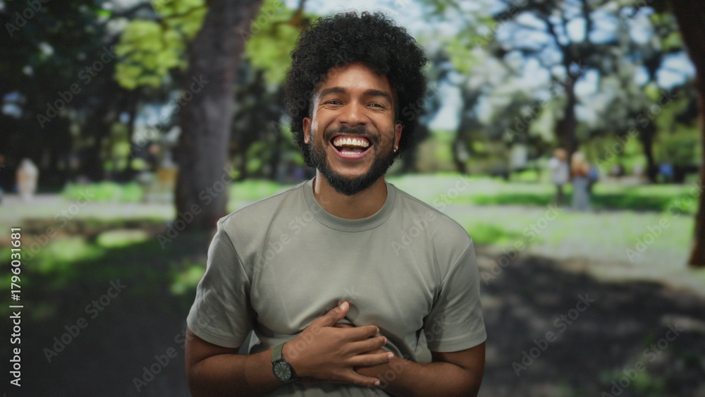 Fototapeta premium Man laughing in a green park with trees and sunlight creating a cheerful outdoor ambiance capturing joyful expression and natural setting.