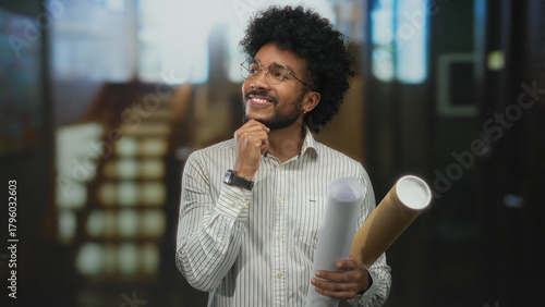 Cuadro en lienzo African american man in a hotel holding blueprints indoors, smiling thoughtfully in a modern environment, showcasing creativity and planning in architectural design