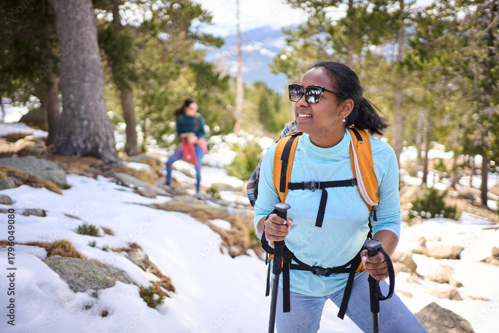 Naklejka premium Female hiker enjoying a snowy mountain forest trail, equipped with backpack and trekking poles, embracing the serene winter landscape
