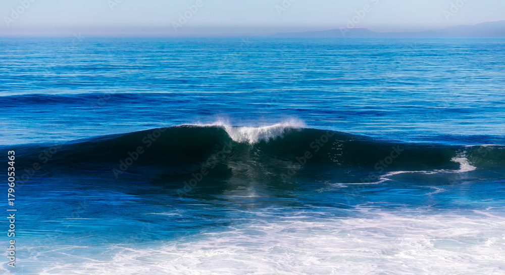 Fototapeta premium Beautiful blue wave crashing in the Pacific Ocean off the California coast in La Jolla with mountains in the background