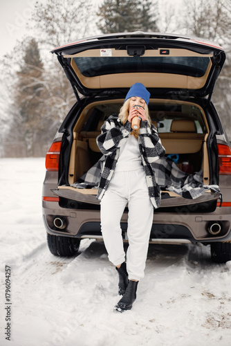 Portrait of a woman standing near open car's trunk in winter forest