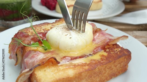 Cutting into a poached egg on toast with crispy bacon, runny yolk close-up