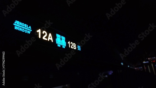 Illuminated seat number sign inside public transportation showing seats 12A and 12B displayed with bright icons and bilingual labels in a dark cabin environment