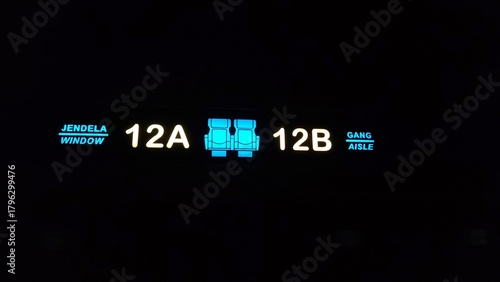 Illuminated seat number sign inside public transportation showing seats 12A and 12B displayed with bright icons and bilingual labels in a dark cabin environment