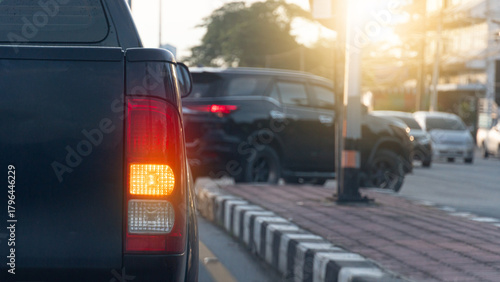 Rear side of pickup car black color with turn on signal right. Park to wait for a U-turn. Car in front is about to make a U-turn. Blurred of many cars are driving by.