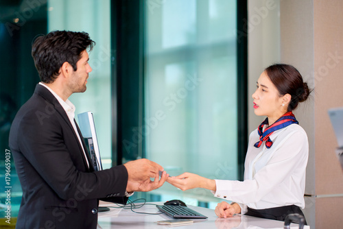 A businessman in black suit show his mobile phone for check in to air ground staff at airport counter check in.