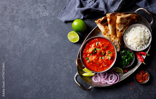 Authentic Indian feast: chicken tikka masala with rice, naan, lime and spices. Grey background. Copy space. Top view.