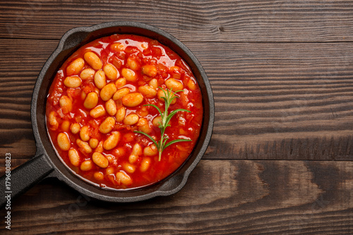 Baked bean dish in cast iron pan on wooden background.	