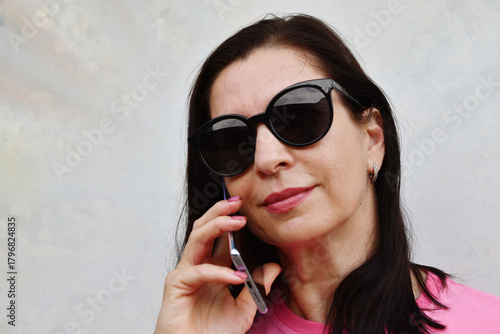 Portrait of Caucasian brunette woman in pink t-shirt and sunglasses talking on the phone.