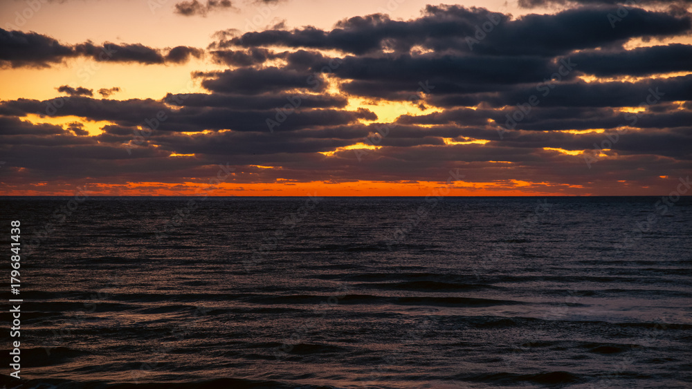 Fototapeta premium Sunrise clouds over the Black Sea in Obzor, Bulgaria with layered dark formations and glowing warm light on the horizon above calm waves