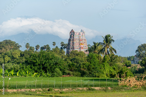 A colorful temple in Kallidaikurichi rises amidst greenery, with mountains and blue sky forming a peaceful backdrop.
