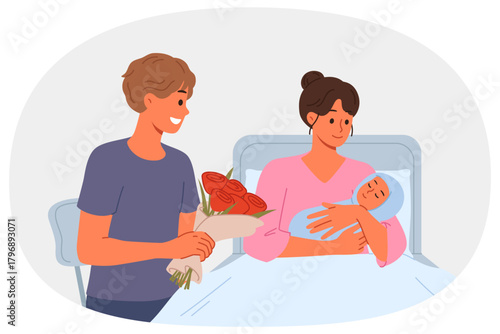 Woman given birth lies in hospital bed, showing baby to happy father with flowers. Girl who has given birth and happy man rejoicing at nascency of son or daughter after long pregnancy