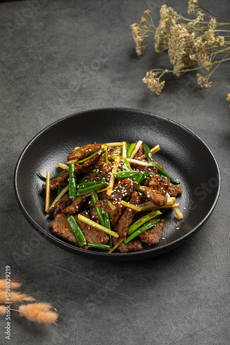 Savory beef stir fry with green onions, sesame and vegetables served in a black bowl
