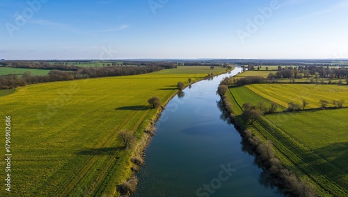 Aerial view of lush green meadows alongside a winding river, showcasing seasonal change
