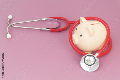 Piggy bank and red stethoscope on purple background. Copy space for text.
