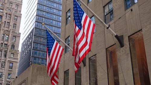 Two big American flag hang on the façade of the high-rise. Low angle view. Patriotic symbols of New York.