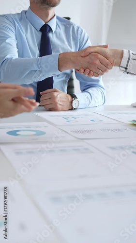 Business partnership success concept with handshake in modern office, financial charts, graphs and laptop on desk representing teamwork, agreement and corporate growth