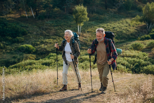 Athletic elderly man and woman hike in hilly autumn countryside